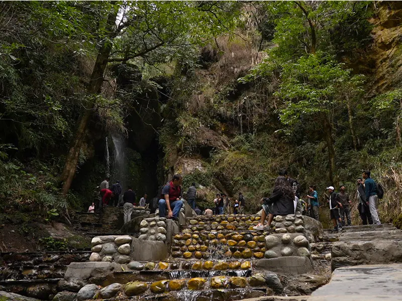 Jibhi Waterfall flowing through rocks surrounded by green forest.